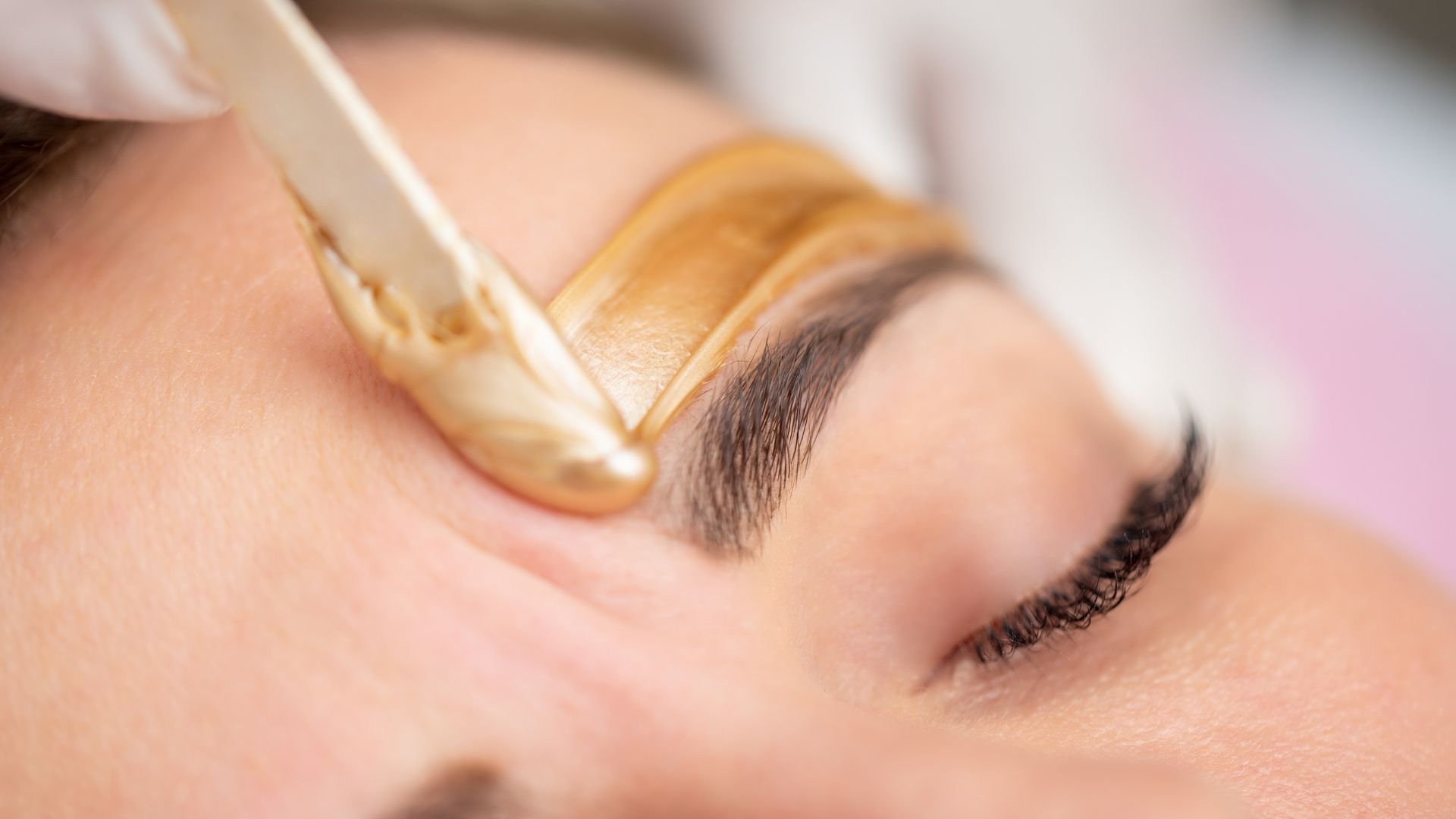 Close-up of eyebrow waxing with golden wax being applied