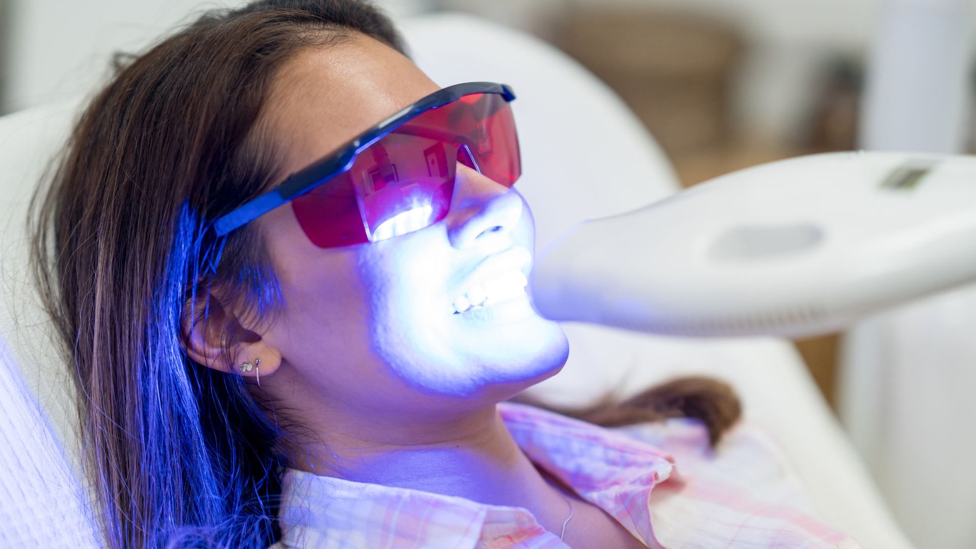 Dental patient receiving teeth whitening treatment with blue UV light
